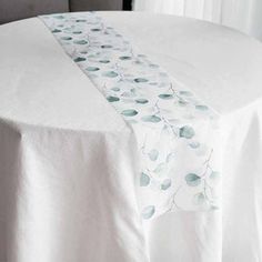 a white table cloth with green leaves on it and a black chair in the background