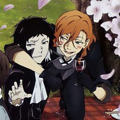 three people sitting at a picnic table with wine glasses in their hands and flowers around them