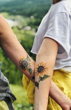 two people holding hands with sunflower tattoos on their arms and the other one has a flower tattoo on her left arm