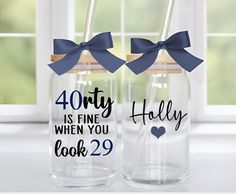 two personalized glass tumblers with blue bows on the top and one saying forty is fine when you look 29