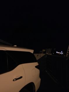 a white car parked on the side of a road next to a bridge at night