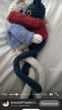 a crocheted stuffed animal laying on top of a white bed with a red and blue scarf around it's neck