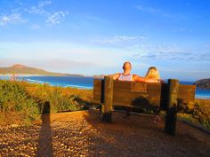 two people sitting on a bench looking out at the ocean