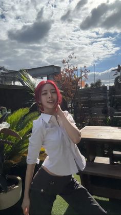 a woman with red hair is posing in front of a picnic table and bench on a sunny day