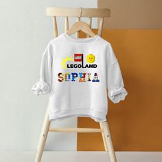 a white legoland sweatshirt hanging on a wooden chair in front of a yellow wall