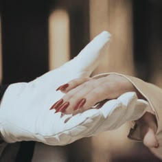 a woman's hand with red nail polish on her nails is being held up by a man in a suit