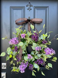 a wreath with purple flowers and green leaves hangs on the front door's black door