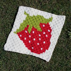 a crocheted square with a strawberry on it sitting in the grass next to some flowers