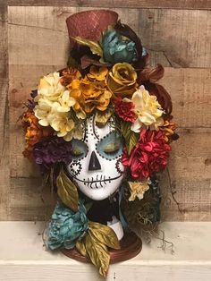 a skull with flowers on it's head is sitting on a wooden wall next to a