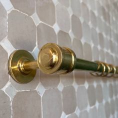 a close up of a gold and green handle on a shower curtain rod with hexagonal tiles in the background