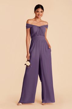 a woman in a purple off the shoulder jumpsuit with her hands on her hips