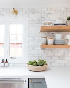 a white kitchen with open shelving above the sink and dishes on the counter top