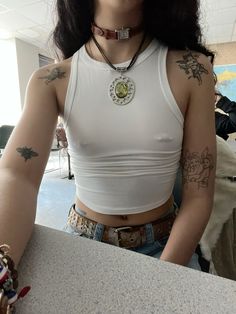 a woman with tattoos on her arm wearing a white tank top and belt around her waist