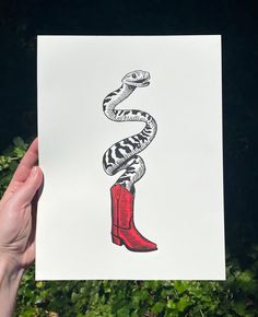 a hand holding up a card with a snake on the top and red boots below it