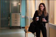 a woman is walking down the hallway holding a cup of coffee and listening to music