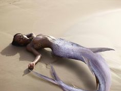 a woman laying on top of a sandy beach next to a purple mermaid tail and head