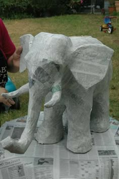 an elephant made out of newspaper sitting on top of a table next to a person