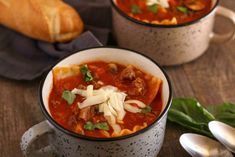 two bowls of soup on a table with spoons next to it and bread in the background