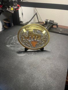 a gold belt buckle sitting on top of a table next to a printer and some wires