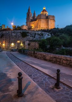 an old castle sits on top of a hill next to a stone wall and walkway