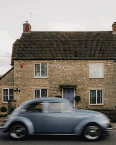 an old car driving past a brick house