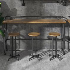 three stools and a table in front of a concrete wall with metal pipes on it