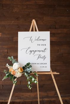 a sign with flowers and greenery on it sitting in front of a wooden wall