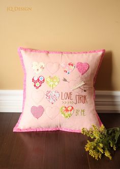 a pink pillow sitting on top of a wooden floor next to a vase filled with flowers