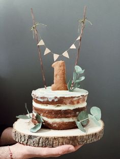 a person holding a cake on top of a tree stump with leaves and bunting