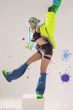 a woman with green hair and glasses on top of a white block in front of paint splatters