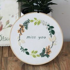 a cross - stitch hoop with the words miss you on it next to a potted plant