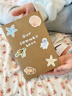 a baby holding a book with stickers on it's cover that says, our summer book