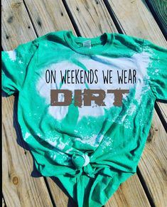 a green shirt with the words on weekend we wear dirt printed on it sitting on a wooden table