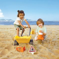 two young children playing in the sand at the beach with toy vehicles and shovels