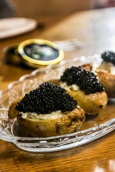 three baked potatoes with black cavias on them sitting on a glass platter