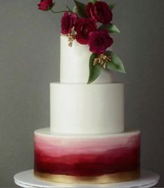 a three tiered cake with red flowers on top and white icing, sitting on a plate