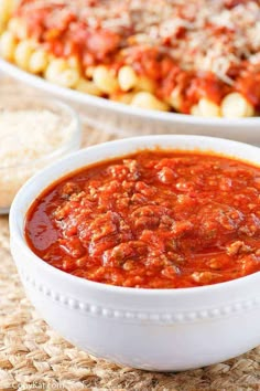 two bowls filled with pasta and sauce on top of a woven place mat next to breadcrumbs