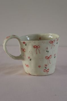 a white cup with pink bows on it sitting on top of a table next to a wall