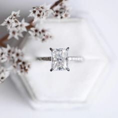 an engagement ring with a princess cut diamond on it and flowers in the foreground