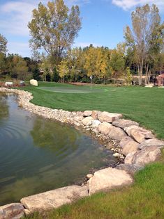 a pond in the middle of a grassy area with rocks and grass around it, near a golf course