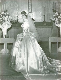 an old black and white photo of a woman in a wedding dress standing next to a church pew