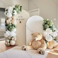 a teddy bear sitting on the floor next to balloons and greenery in front of it