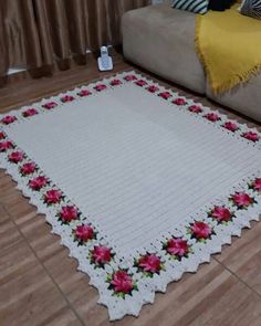 a white rug with pink flowers on it in the middle of a floor next to a couch