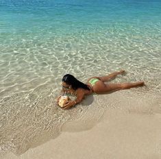 a woman laying on top of a sandy beach next to the ocean holding a ball