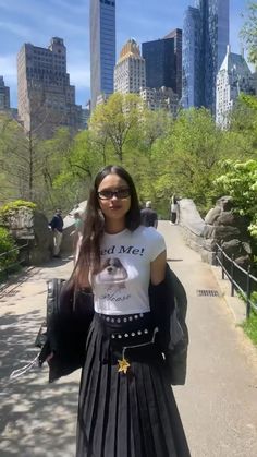 a woman in a skirt and t - shirt is walking down the street with her hand on her hip