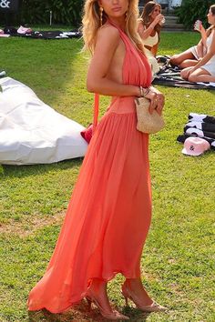 a woman in an orange dress is standing on the grass with other people around her