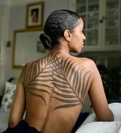 a woman sitting on top of a bed with a tattoo on the back of her body