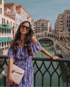 a woman in a blue dress standing on a balcony next to a river and buildings