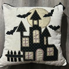 a black and white pillow with an embroidered castle on the front, bats flying over it