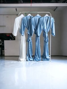 three blue robes hanging on a rack in a room with white walls and flooring